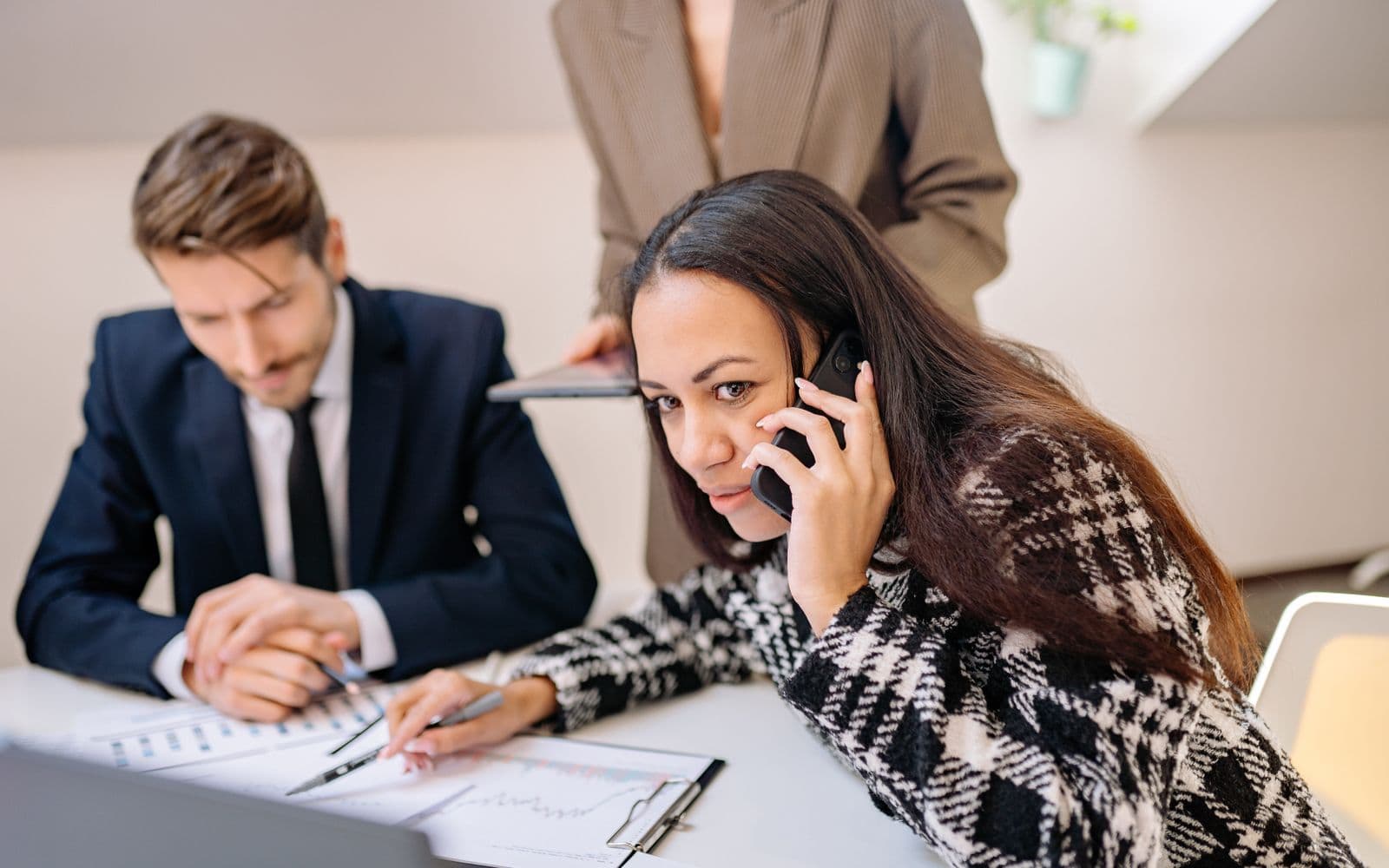 Two colleagues at a desk, one on a call while reviewing paperwork